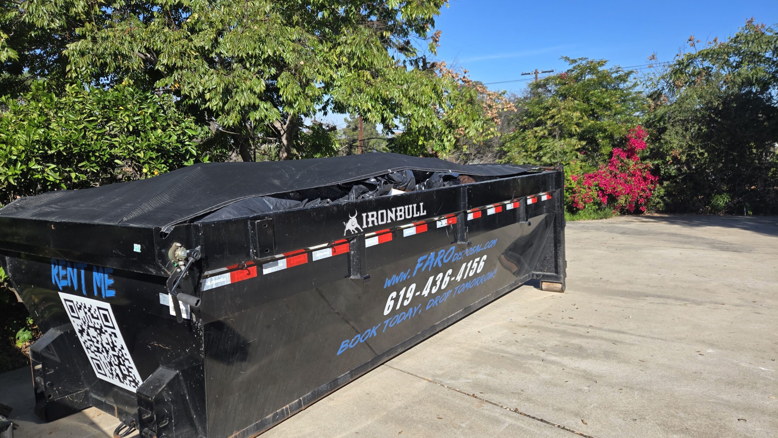 Large black dumpster near greenery